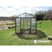 Grandio Elite Greenhouse lifestyle image shown in a backyard with plants growing next to an open field 